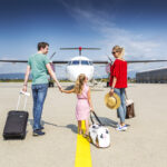 A family of three on the airport runway in front of an aeroplane