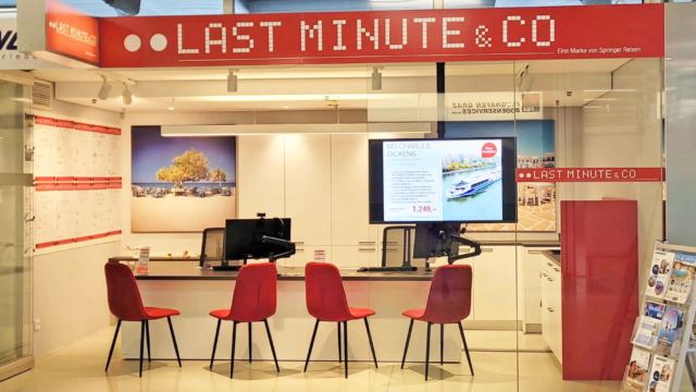 Ansicht der Reisebürokoje am Flughafen mit roten Stühlen.