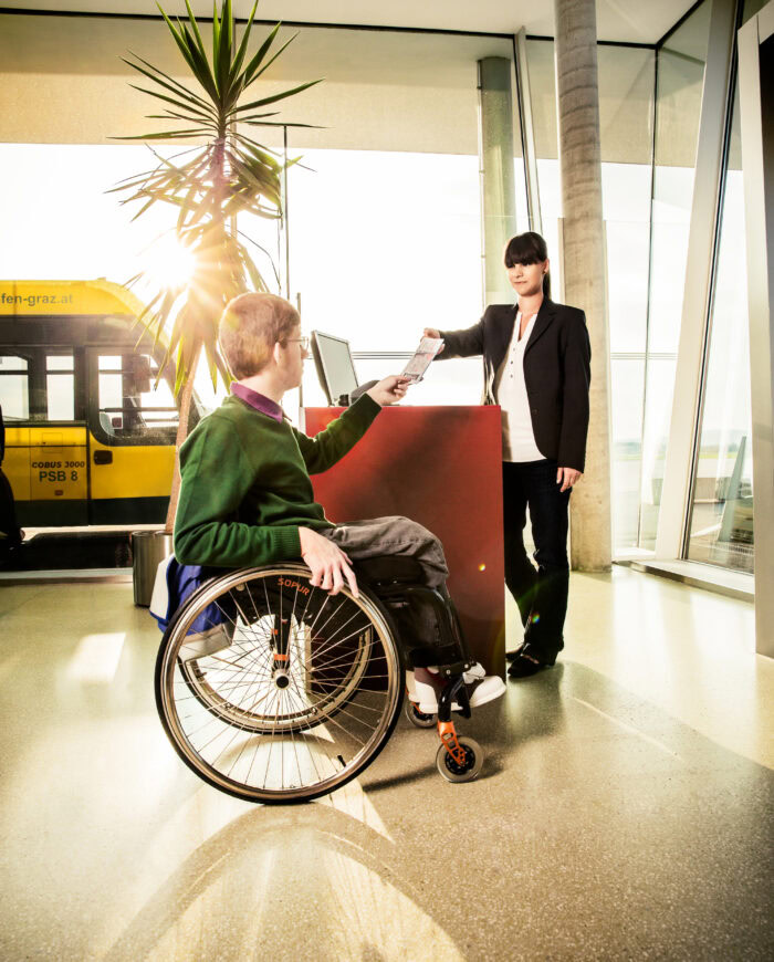 Mann im Rollstuhl und Mitarbeiterin beim Boarding am Gate