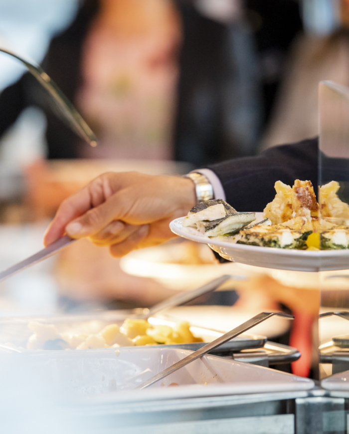 Hand gibt Essen von Buffet auf Teller