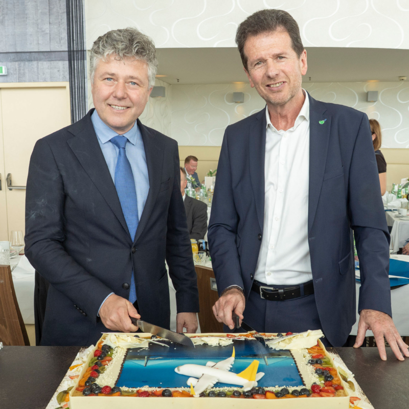Two men in suits cutting a cake.