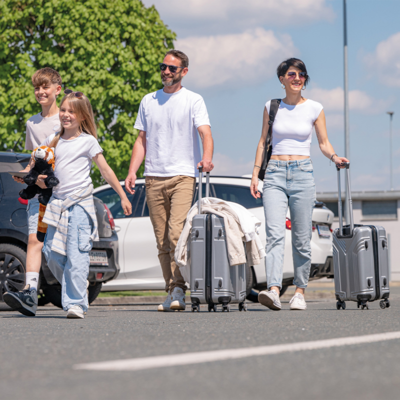 Eine Familie mit Gepäck, die vom Parkplatz zum Flughafen geht.
