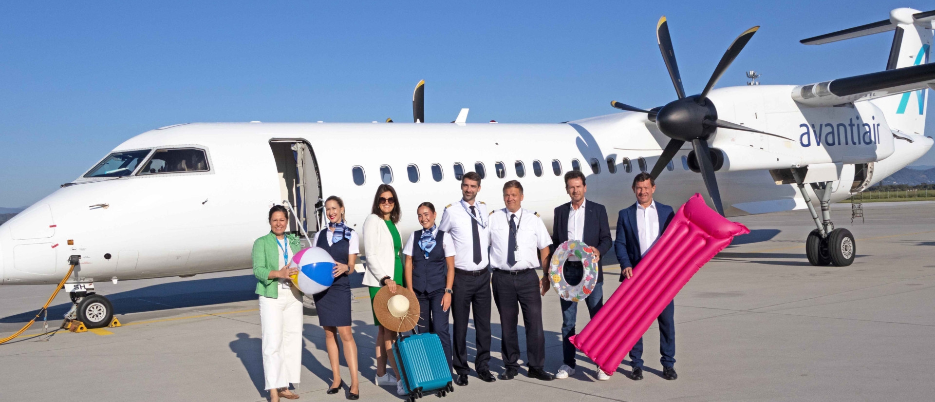 Gruppenfoto mit Strandutensilien vor einem Flugzeug.