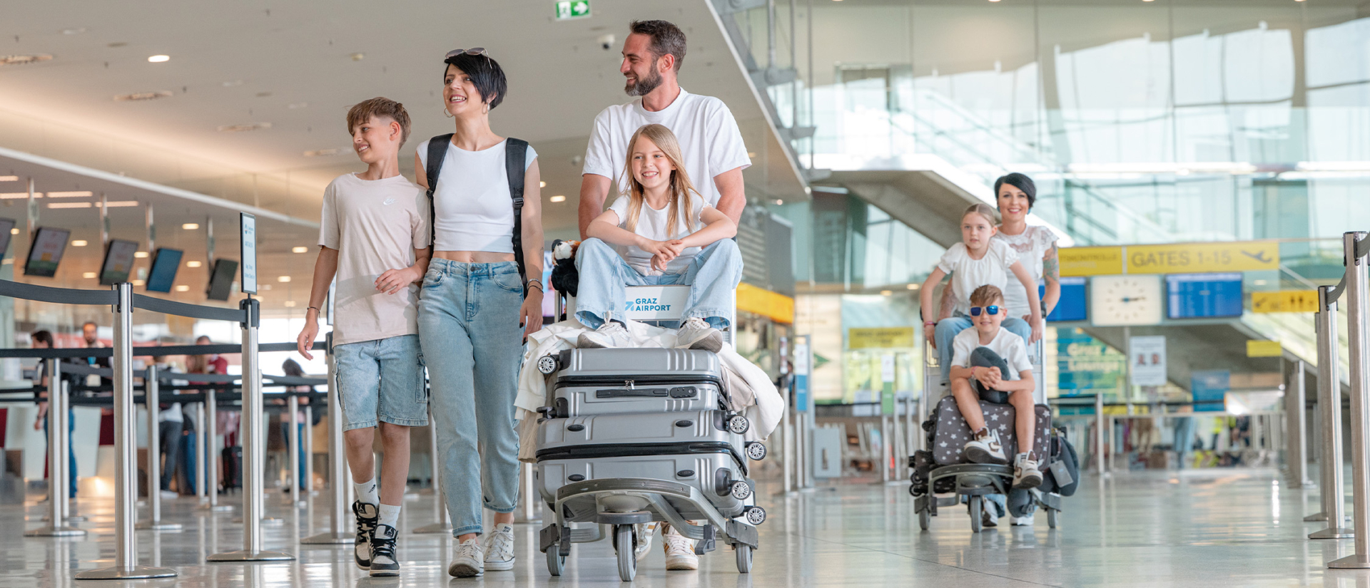 Zwei Familien mit Koffern auf dem Gepäckwagen gehen durch das Flughafen-Terminal.