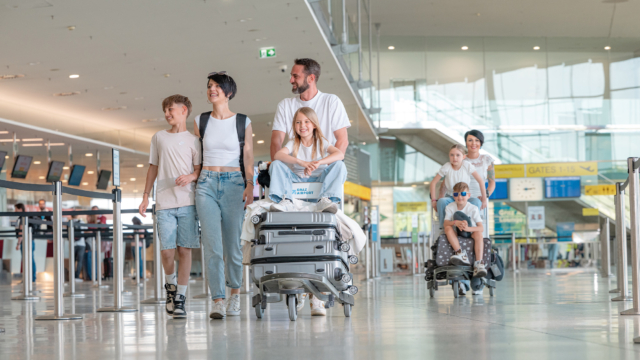 Foto: 5komma5sinne/Rene Strasser Zwei Familien mit Koffern auf dem Gepäckwagen gehen durch das Flughafen-Terminal.