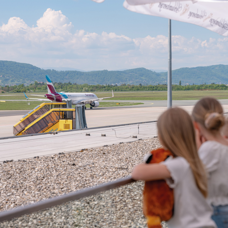Eine Gruppe von Kindern beobachtet von einer Terrasse aus ein Flugzeug.