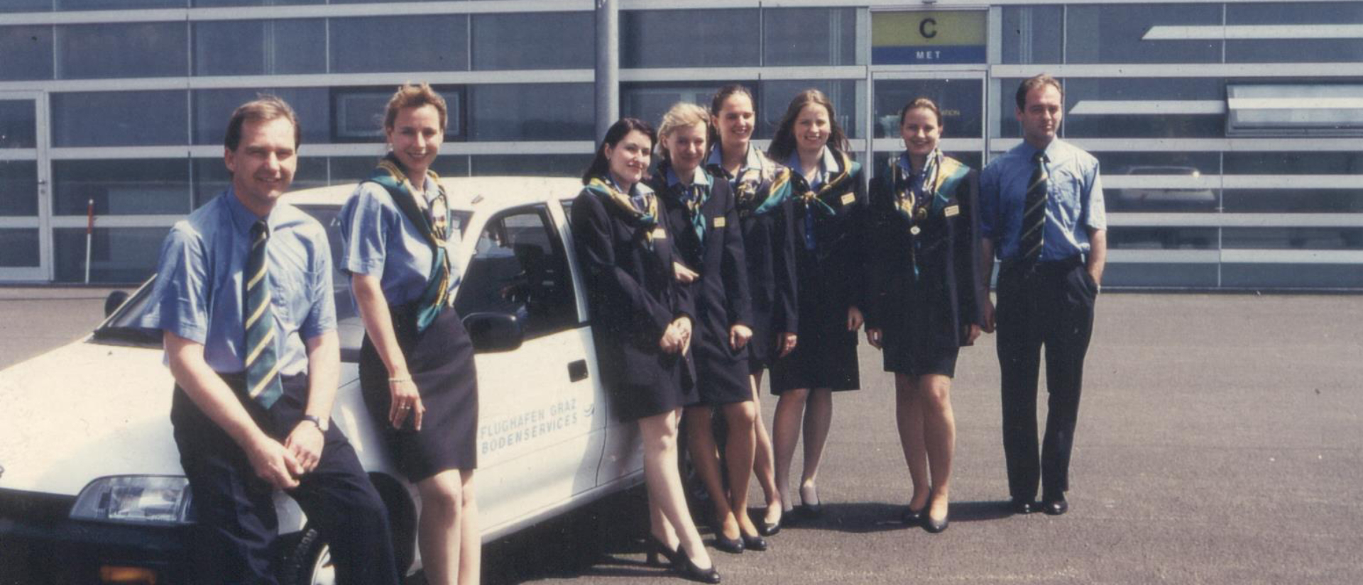 Personen in Uniformen lehnen an einem weißen Auto.