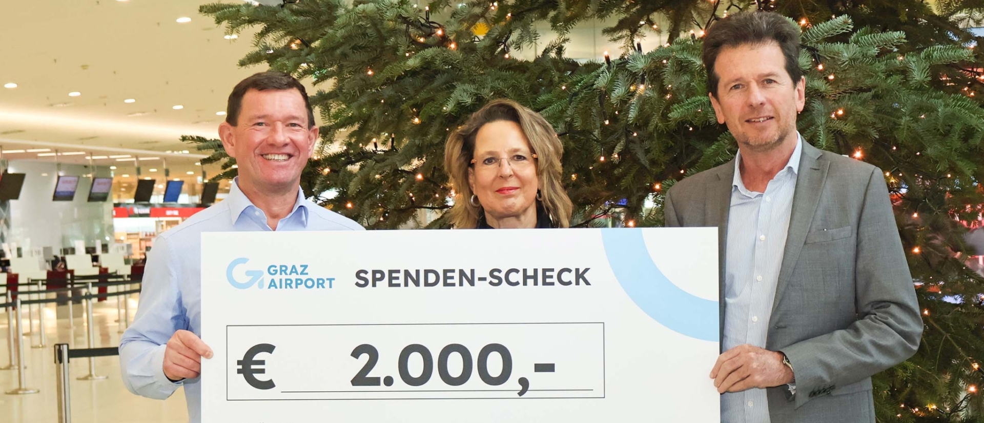 3 Personen mit Spendenscheck vor Weihnachtsbaum