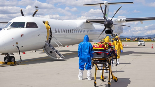 Personen mit Schutzanzügen vor einem Propellerflugzeug.